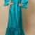 Model wearing a turquoise satin dress with flared sleeves and ruffle hem, hands on hips, front view.